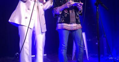 Two people stood on a stage with a card in hand announcing the 2022 AMA UK award nominees