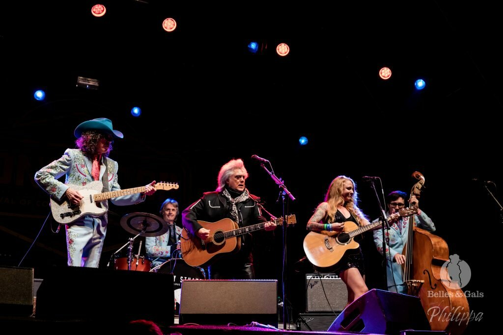 Musicians on stage performing at the long road festival. A red headed female guitarist and vocalist and two male guitarists are performing