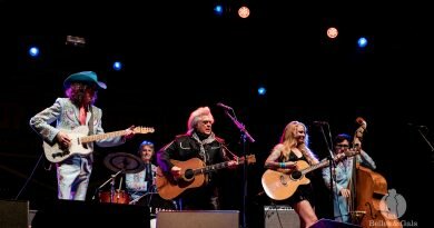 Musicians on stage performing at the long road festival. A red headed female guitarist and vocalist and two male guitarists are performing