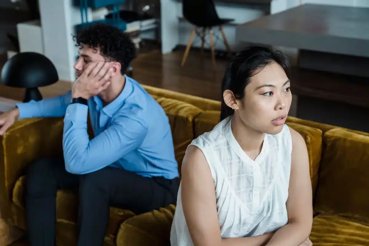 A couple sitting together on a couch, one person reaching toward the other in a gesture of connection and reconciliation