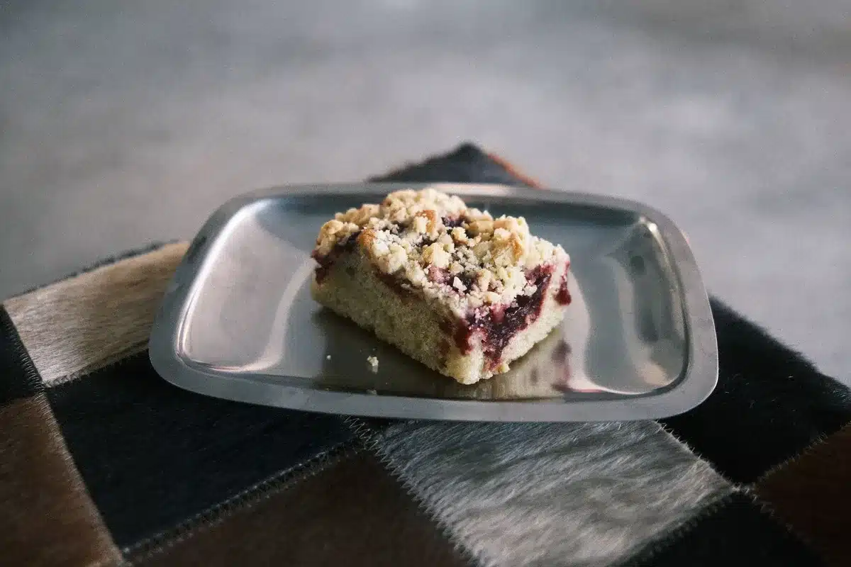 Hands sprinkling golden crumble mixture over fresh fruit in a baking dish
