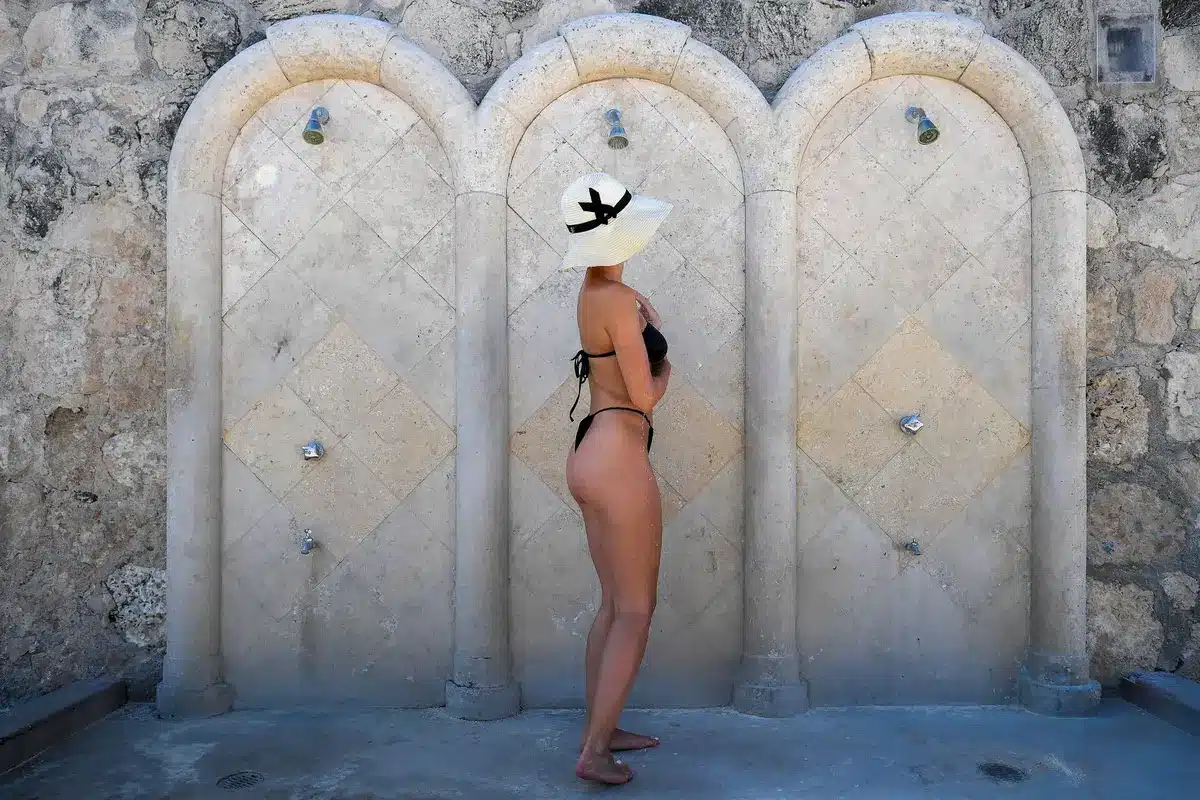 Woman in leopard-print bikini and designer sunglasses walking on a sunny beach