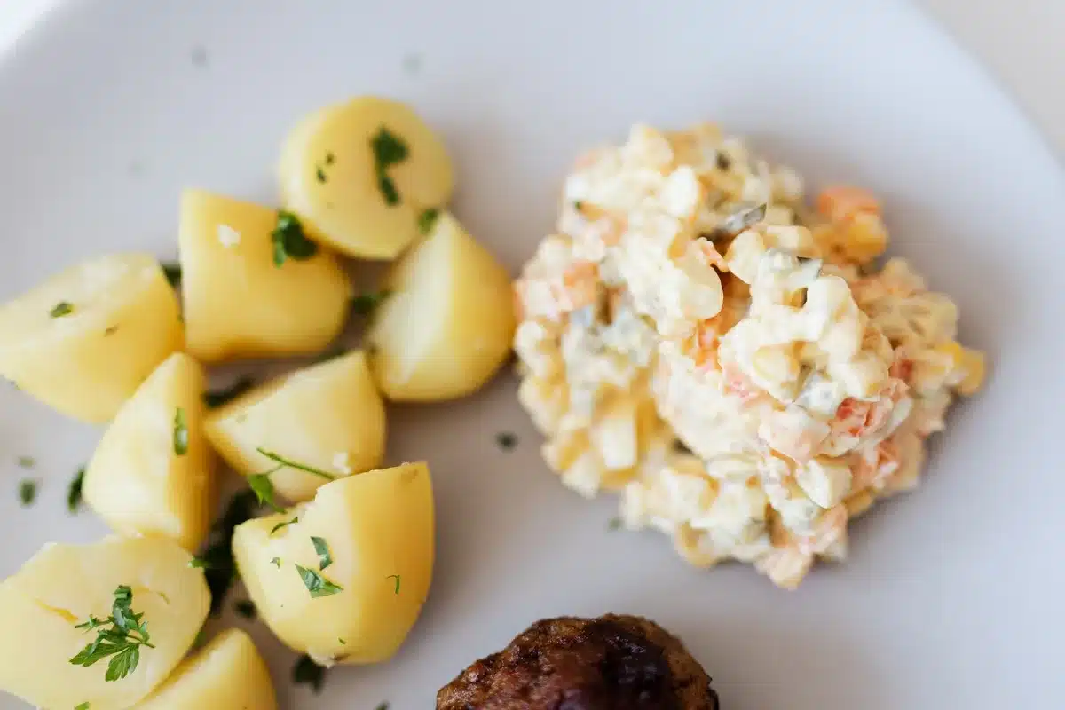 Colorful potato salad with diced potatoes, apple, eggs and fresh herbs in a white bowl
