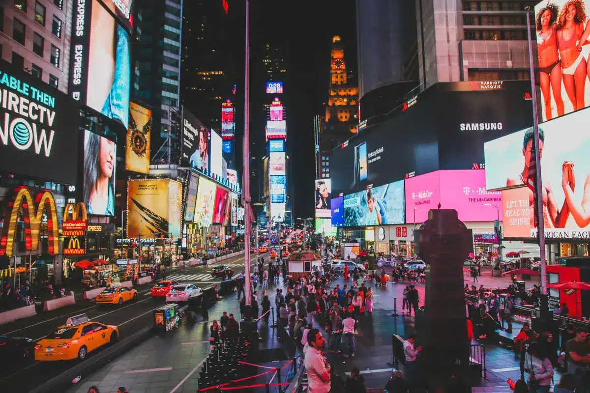 Person in black leather outfit walking through Times Square at night with neon lights and crowds