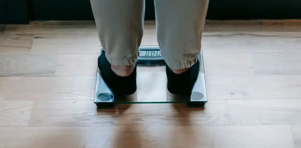 Person standing on a bathroom scale with measuring tape and health tracking items nearby