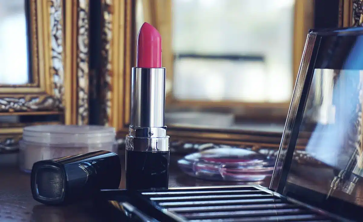 Makeup products and brushes arranged on a vanity mirror with athletic setting in background