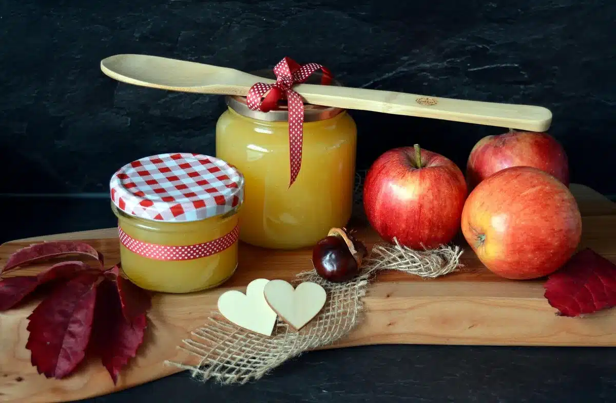Jam cooking in a preserving pan with a wooden spoon, golden bubbling mixture, kitchen counter setting