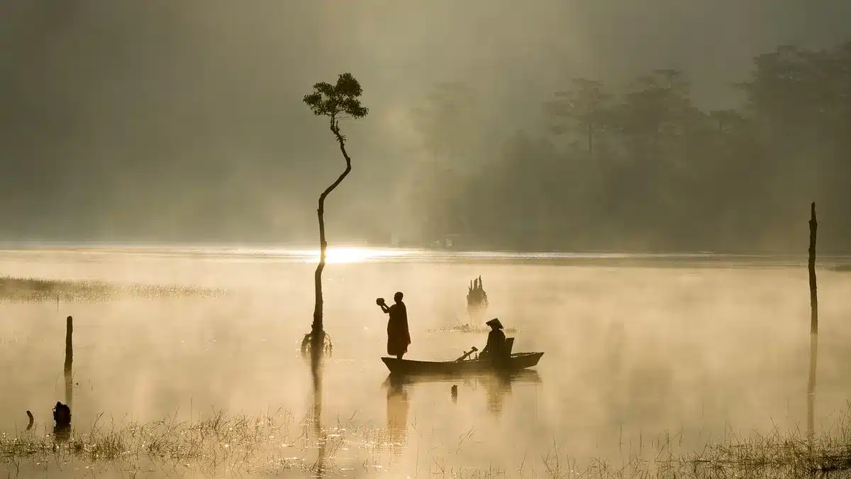 Silhouette of a person on a foggy coastal dock beside a small fishing boat